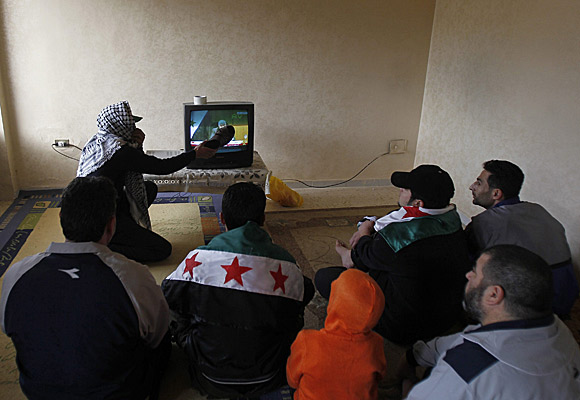 A Syrian refugee hits the television set with a shoe at a temporary home in Amman, Jordan, as other refugees watch a news conference held by Syrian Foreign Minister Walid Moallem.