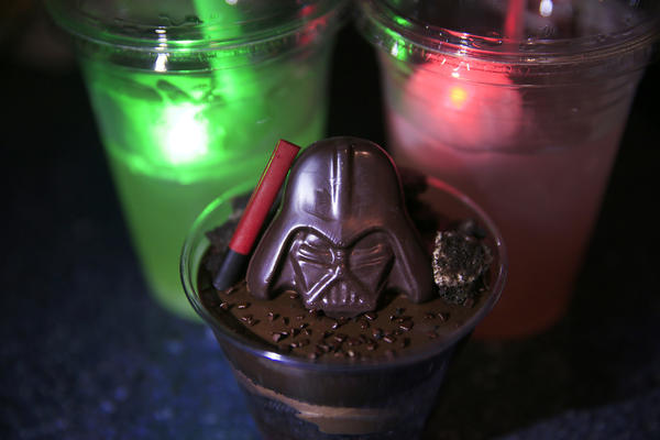 A Darth by Chocolate desert, center, next to The Dark Side drink, on right, and the Light Side drink. It includes a souvenir light-up Millennium Falcon as featured during the media preview of Star Wars Season of The Force at Disneyland.