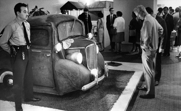 A museum guard stands behind artist Edward Kienholz's "Back Seat Dodge '38."