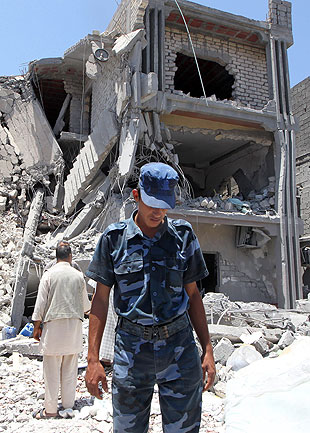 A Libyan policeman inspects rubble in front of a damaged house.