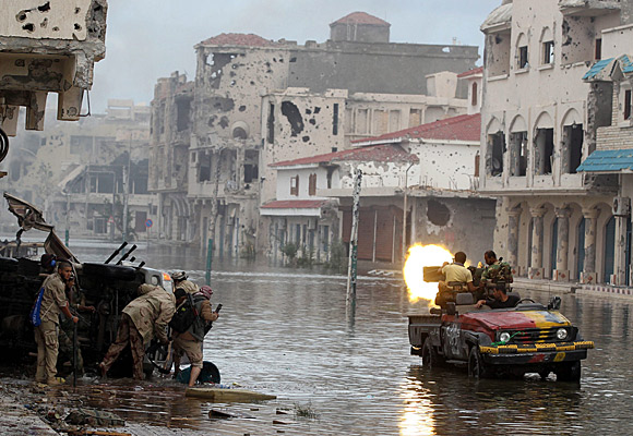 Libyan revolutionaries fire from a street flooded by broken pipes in Surt.