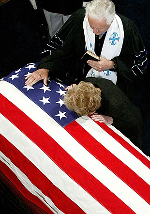 The Rev. Michael Wenning stands by as Nancy Reagan bends over the casket of her husband.