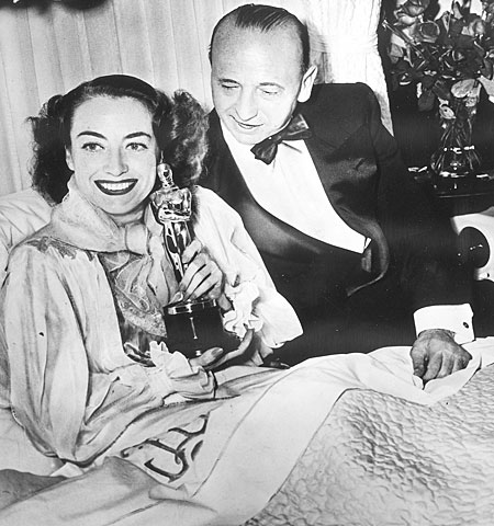 Joan Crawford, too ill to attend the ceremonies, poses at home with her Oscar for "Mildred Pierce" and the film's director, Michael Curtiz.