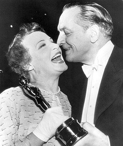 Shirley Booth laughs heartily as actor Fredric March prepares to give her a kiss on the cheek after she was presented with an Oscar.