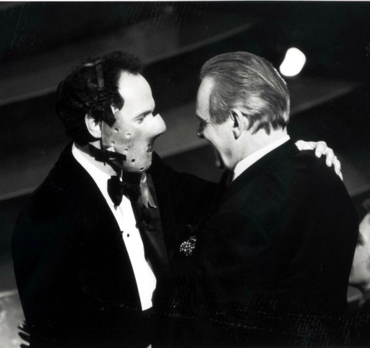 Billy Crystal, in a mask like Hannibal Lecter was forced to wear, greets Anthony Hopkins on stage.
