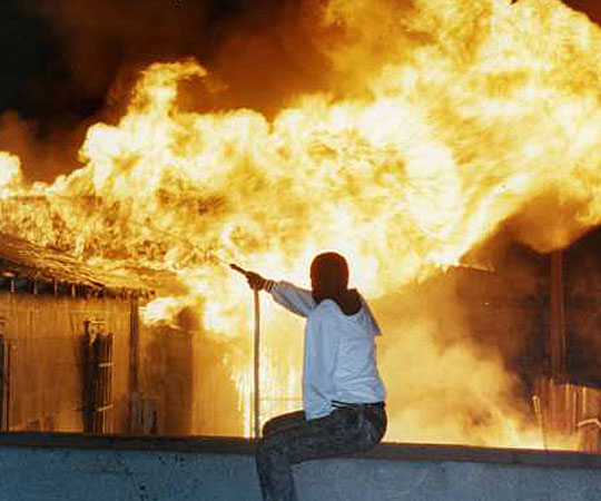 A resident vainly attempts to fight a raging fire at 79th Street and Normandie Avenue using a garden hose. (April 29, 1992)