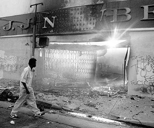 At sunrise, a lone pedestrian walks by burned-out shell of a J.J. Newberry building at Vermont Avenue near 59th Street. (April 30 1992)