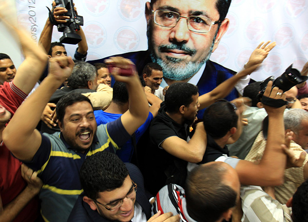 Members of the presidential election campaign of Muslim Brotherhood's Freedom and Justice Party candidate Mohamed Morsi, depicted in poster, celebrate upon the announcement of his victory in a historic election, at their headquarters in Cairo.