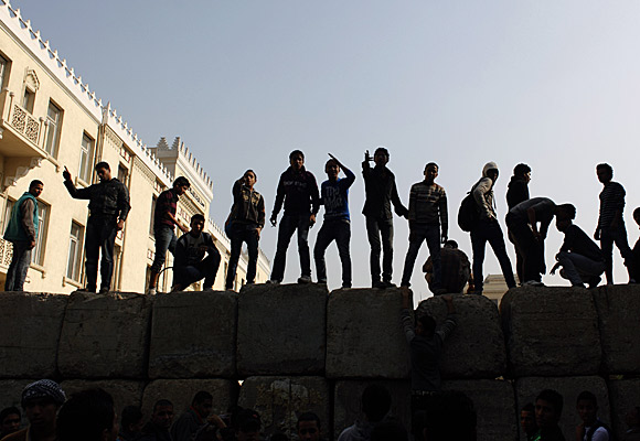 Protesters stand atop a barrier put up by the military to block a road near Tahrir Square in Cairo.