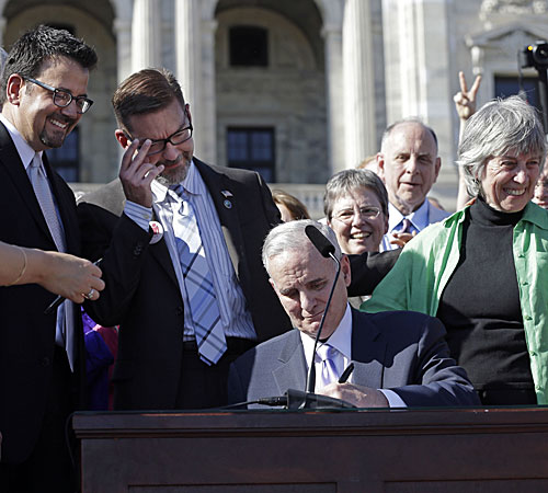 Minnesota Gov. Mark Dayton signs the gay marriage bill in front of the state Capitol. Sen. Scott Dibble, second from left, and Rep. Karen Clark, right, both gay lawmakers and sponsors of the bill, are among those watching the signing.