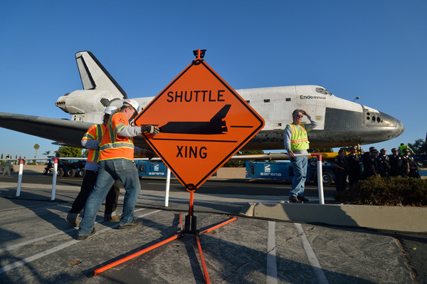 Work crews set up a sign as the Space Shuttle Endeavour makes its way to the Forum enroute to the California Science Center on Saturday.