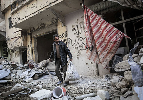 A man gathers belongings from his home in Aleppo, damaged by fighting between Syrian rebels and government forces.
