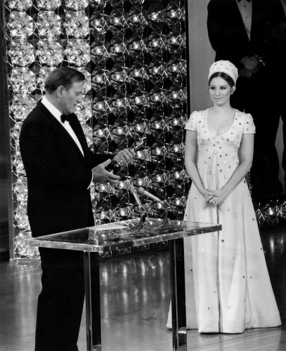 John Wayne accepts his Oscar as presenter Barbra Streisand looks on.